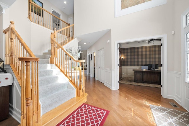 staircase featuring a high ceiling, wood finished floors, a decorative wall, a wainscoted wall, and a ceiling fan