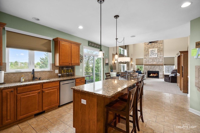 kitchen with stainless steel dishwasher, a sink, a fireplace, a center island, and tasteful backsplash