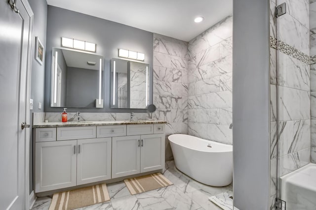 full bath with marble finish floors, a freestanding bath, double vanity, tile walls, and recessed lighting
