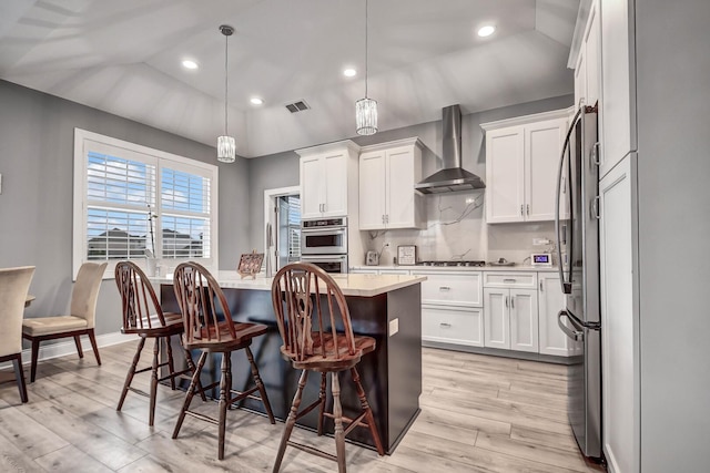 kitchen with a kitchen island, wall chimney range hood, light countertops, a kitchen bar, and white cabinetry