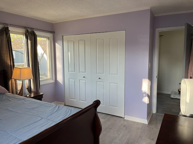 bedroom with wood finished floors, a closet, a textured ceiling, baseboards, and crown molding