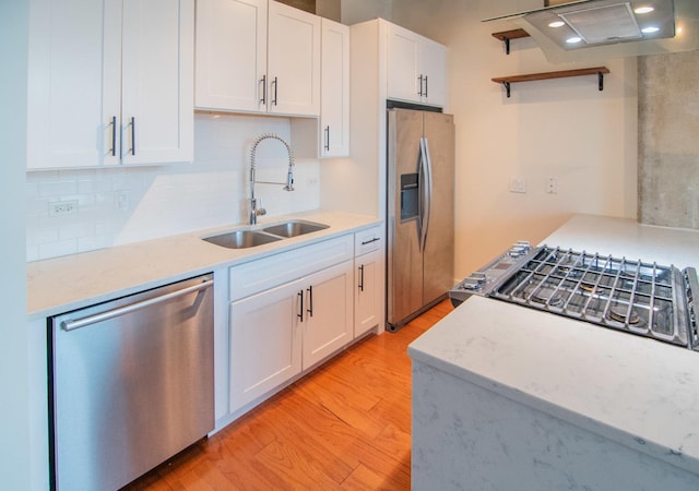 kitchen featuring appliances with stainless steel finishes, a sink, light wood-style floors, white cabinets, and tasteful backsplash