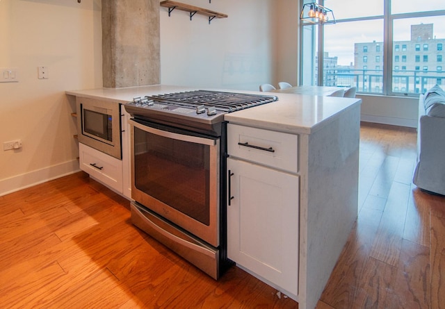 kitchen featuring appliances with stainless steel finishes, a peninsula, white cabinetry, and light wood-style flooring