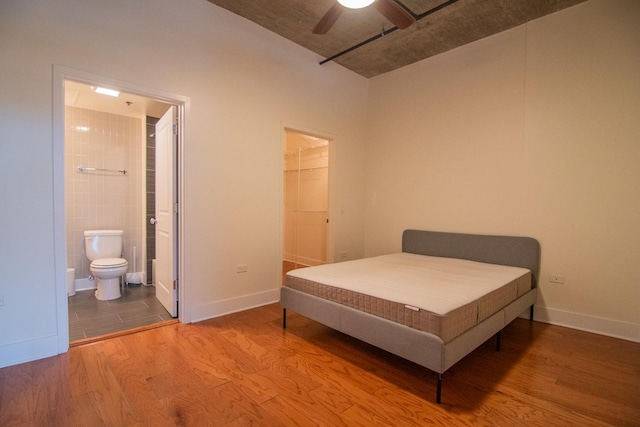 bedroom featuring wood finished floors, baseboards, a walk in closet, and ensuite bath