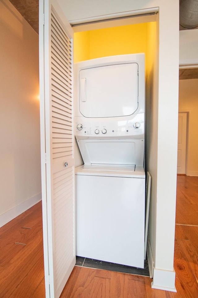 laundry room with estacked washer and dryer, wood finished floors, and baseboards