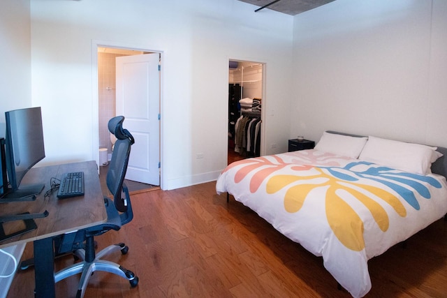 bedroom featuring wood finished floors, a spacious closet, a desk, a closet, and baseboards