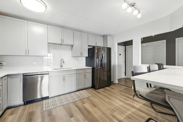 kitchen with appliances with stainless steel finishes, a sink, gray cabinetry, light countertops, and tasteful backsplash