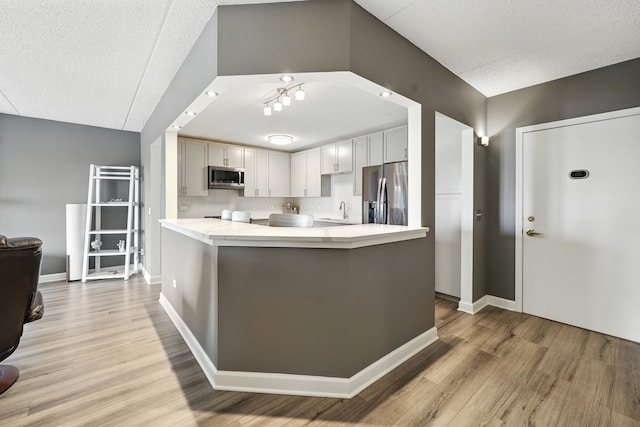 kitchen featuring appliances with stainless steel finishes, light wood finished floors, a textured ceiling, baseboards, and a sink