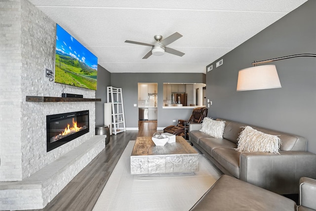 living area featuring wood finished floors, a fireplace, a ceiling fan, and baseboards