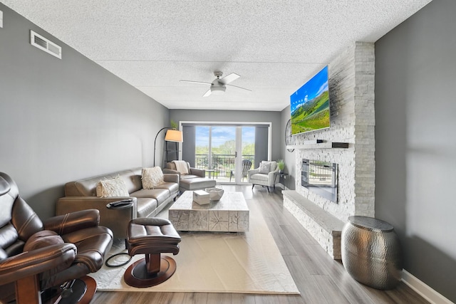 living area featuring ceiling fan, a textured ceiling, wood finished floors, and a fireplace