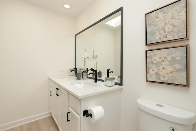 bathroom with wood finished floors, toilet, double vanity, baseboards, and recessed lighting