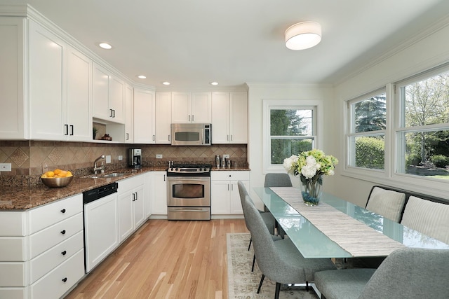 kitchen with appliances with stainless steel finishes, a sink, plenty of natural light, light wood-style flooring, and crown molding