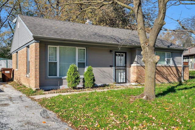 view of front of home featuring brick siding, a front yard, a shingled roof, and a chimney