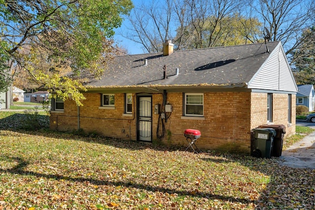rear view of property featuring brick siding, a shingled roof, a chimney, and a yard