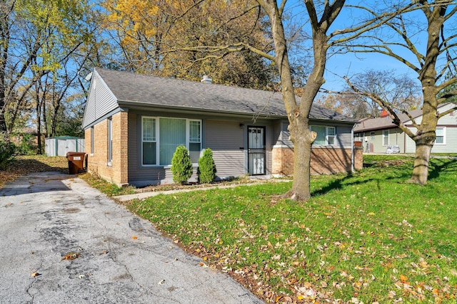 single story home featuring brick siding, a front lawn, asphalt driveway, and roof with shingles