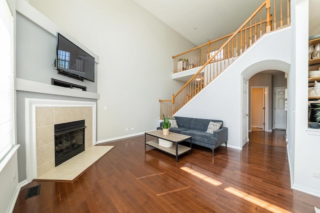 living room with a towering ceiling, wood finished floors, stairs, arched walkways, and baseboards