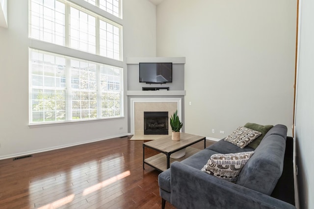 living room featuring a tiled fireplace, a towering ceiling, hardwood / wood-style floors, and baseboards