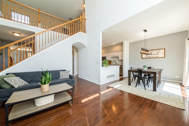 living room featuring wood finished floors, stairway, baseboards, a high ceiling, and arched walkways