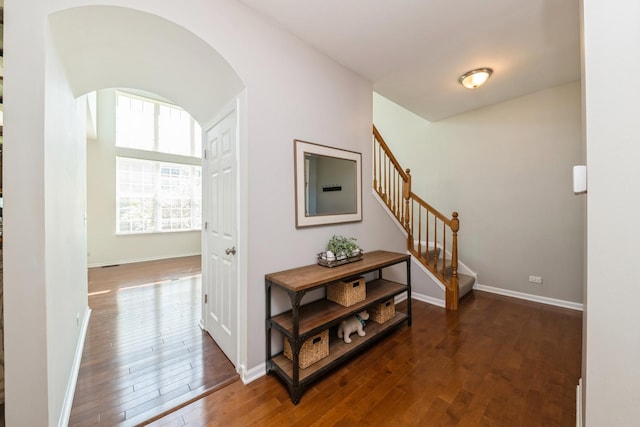 hall with arched walkways, stairway, wood-type flooring, and baseboards