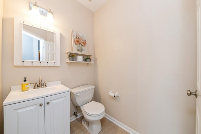 half bathroom featuring toilet, vanity, baseboards, and wood finished floors