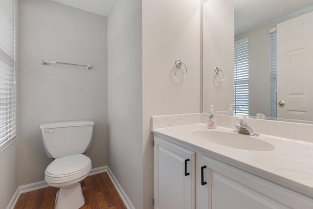 half bath featuring wood finished floors, toilet, vanity, and baseboards