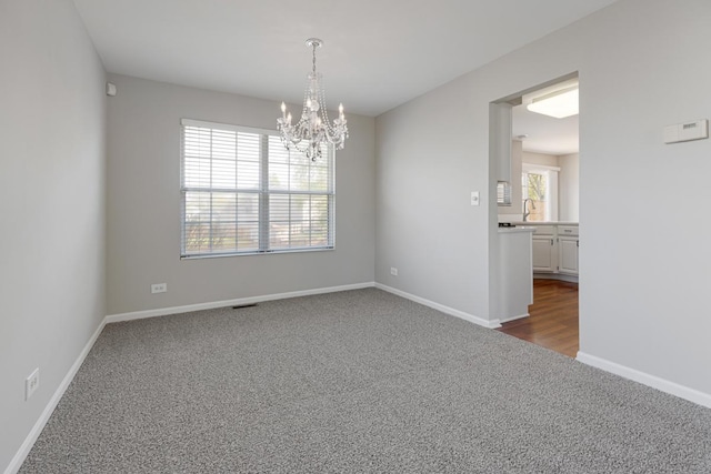 empty room featuring dark carpet, a chandelier, and baseboards