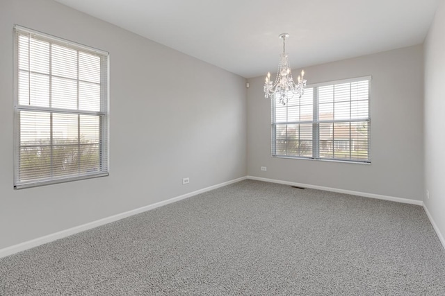 empty room featuring plenty of natural light, a chandelier, baseboards, and carpet floors