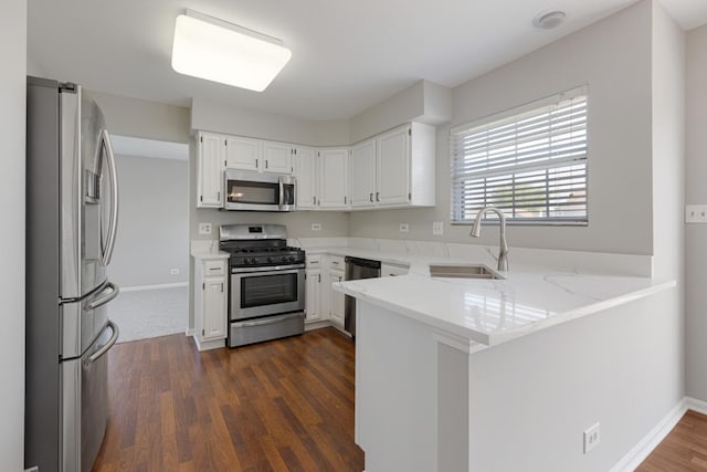 kitchen featuring stainless steel appliances, a sink, a peninsula, white cabinets, and light stone countertops