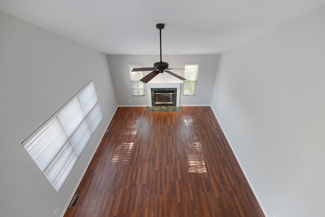 unfurnished living room featuring ceiling fan, a premium fireplace, baseboards, and wood finished floors