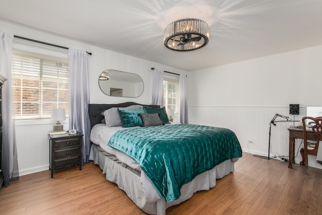 bedroom with light wood-type flooring, a wainscoted wall, and baseboards