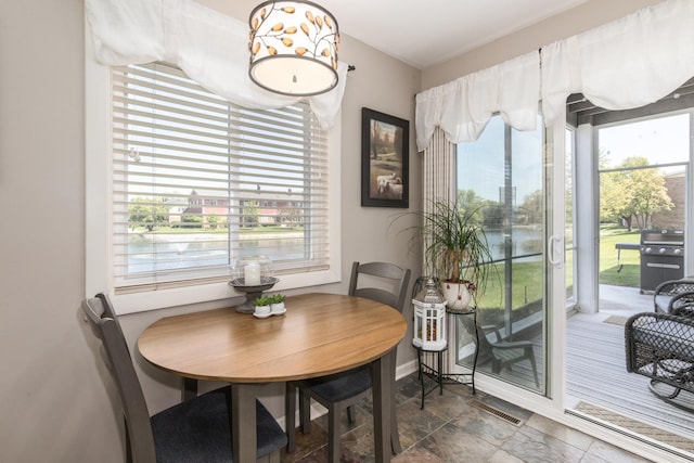 dining area featuring stone finish floors, a water view, and baseboards