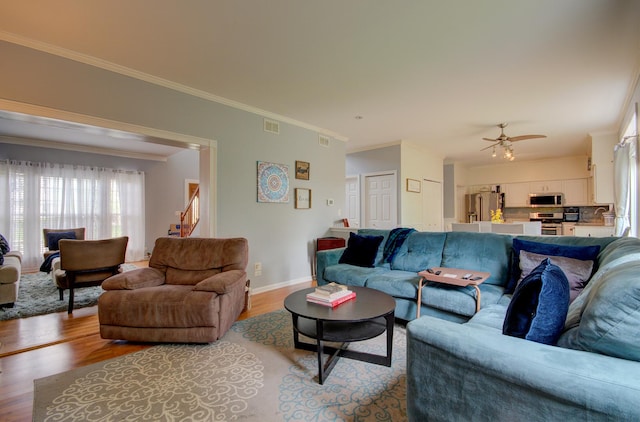 living area with light wood-type flooring, ornamental molding, ceiling fan, and baseboards