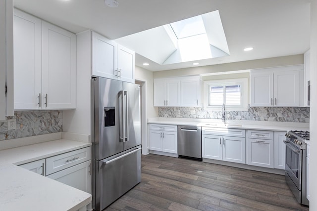 kitchen featuring stainless steel appliances, a sink, a skylight, white cabinetry, and dark wood finished floors