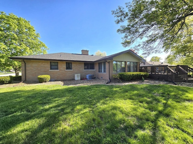 rear view of property featuring brick siding, a wooden deck, a chimney, central AC unit, and a lawn