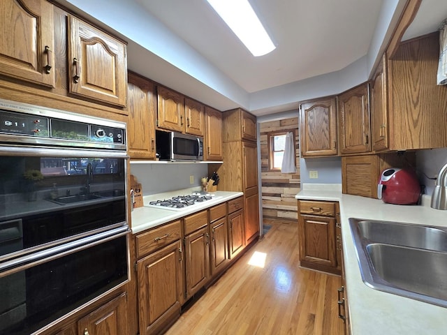 kitchen featuring stainless steel microwave, a sink, white gas cooktop, light wood-type flooring, and light countertops