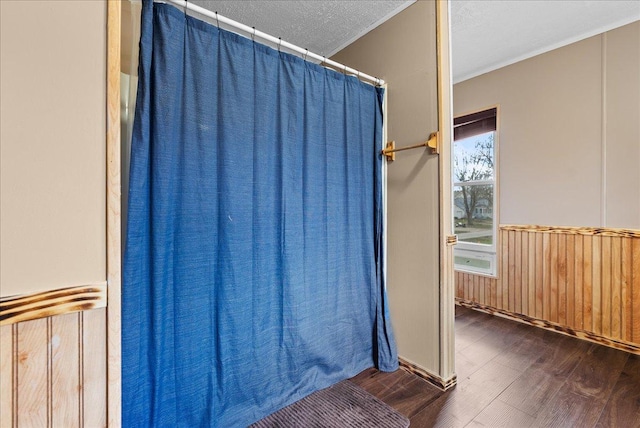 bathroom featuring wood finished floors, a textured ceiling, wooden walls, wainscoting, and crown molding
