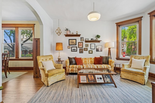 sitting room featuring arched walkways, healthy amount of natural light, wood finished floors, and baseboards