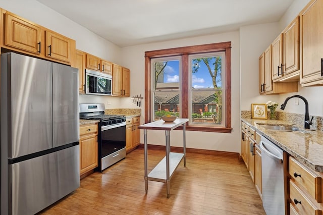 kitchen featuring stainless steel appliances, a sink, light wood-style flooring, light stone counters, and baseboards