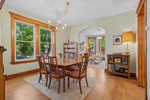dining room with arched walkways, light wood finished floors, a chandelier, and baseboards
