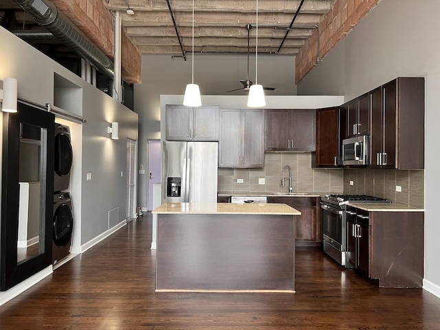kitchen with stainless steel appliances, a high ceiling, stacked washing machine and dryer, light countertops, and a sink