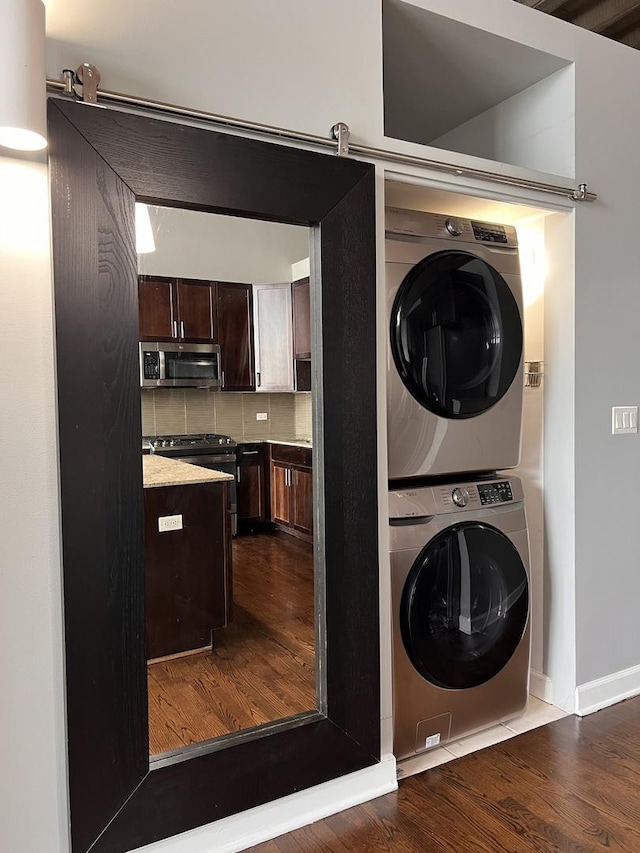 clothes washing area featuring stacked washer / dryer, dark wood-type flooring, and baseboards