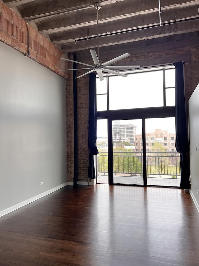 empty room with healthy amount of natural light, ceiling fan, wood finished floors, baseboards, and beamed ceiling