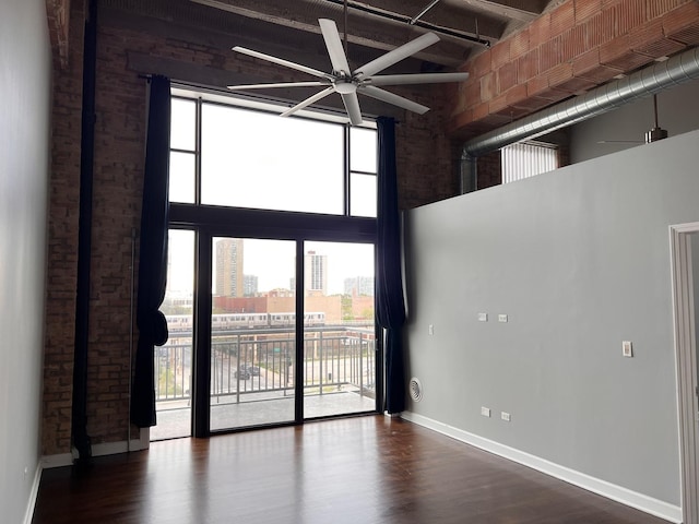 empty room featuring a towering ceiling, a ceiling fan, baseboards, wood finished floors, and a city view
