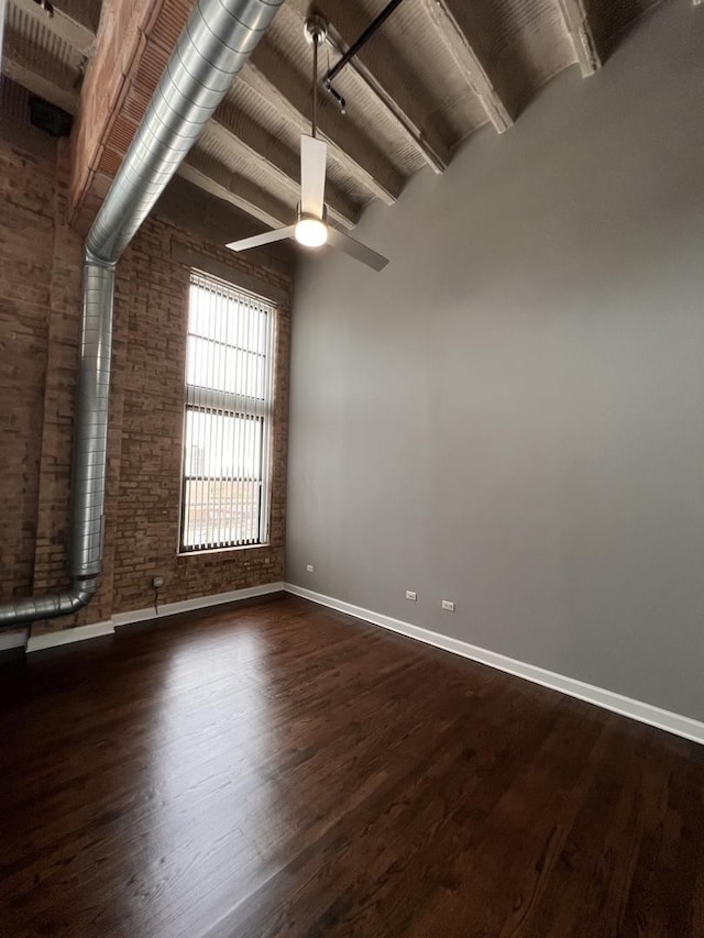 empty room featuring baseboards, brick wall, wood finished floors, beamed ceiling, and ceiling fan