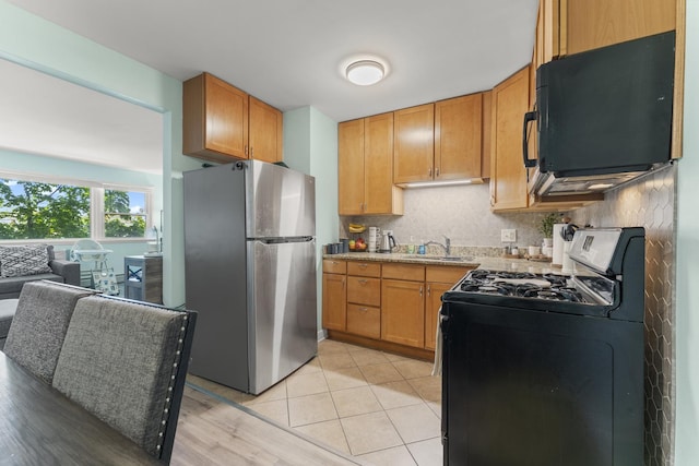 kitchen with freestanding refrigerator, gas range oven, black microwave, a sink, and backsplash