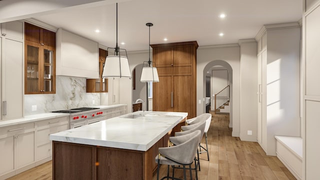 kitchen featuring arched walkways, a kitchen island with sink, decorative backsplash, recessed lighting, and light wood-type flooring