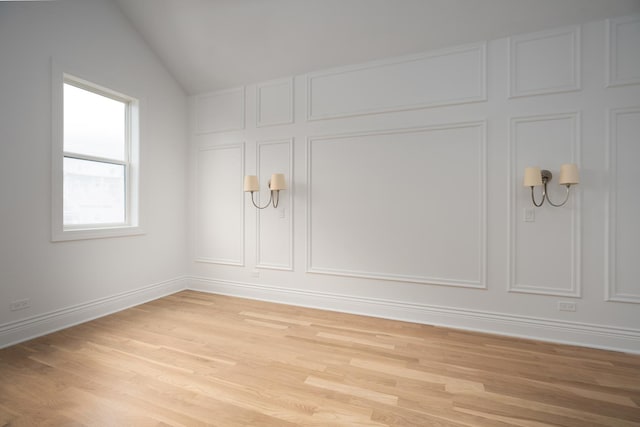 empty room featuring vaulted ceiling, light wood-style flooring, baseboards, and a decorative wall