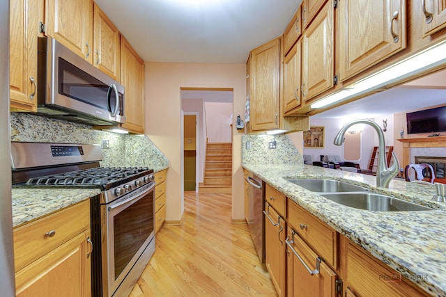 kitchen with stainless steel appliances, a sink, light wood-style floors, light stone counters, and tasteful backsplash