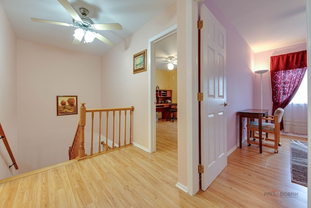 hall with an upstairs landing, wood finished floors, baseboards, and a desk