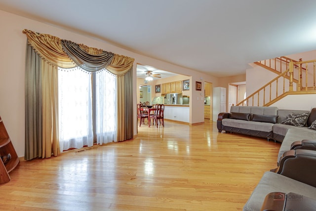 living room with stairway, light wood-style floors, and a ceiling fan
